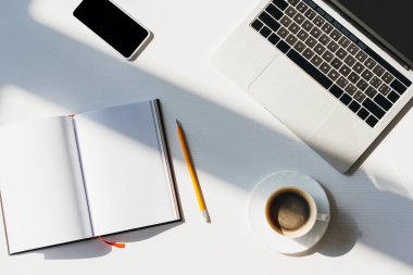 Bilgisayarlı, akıllı telefonlu, not defterli, kalemli ve kahveli boş işyerinin üst görünümü