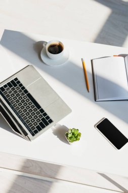 Dizüstü bilgisayarı, akıllı telefonu, not defteri ve güneş ışığında kahve fincanı olan iş yeri