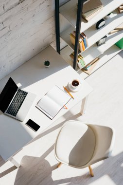 Bilgisayarlı, akıllı telefonlu ve güneş ışığında bir fincan kahveli ev ofisinin üst görüntüsü.