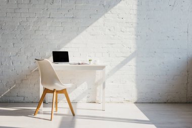 Masalı ev ofisi, sandalye ve güneş ışığında boş ekranlı laptop.