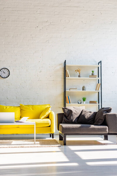 гостиная с желтым диваном, серым креслом, рубашкой и ноутбуком в солнечном свете
