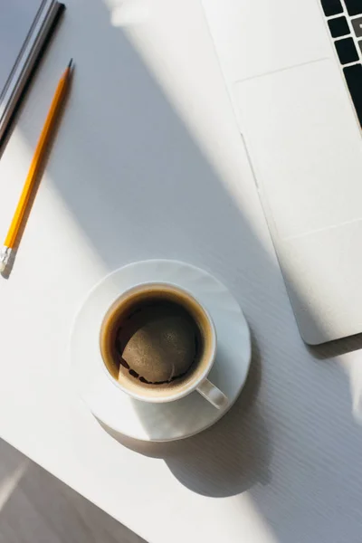 top view of empty workplace with laptop, cup of coffee and pencil in sunlight