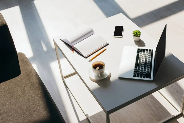 empty workplace with laptop, smartphone, notepad and coffee in sunlight