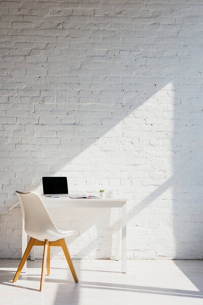 home office with laptop on table and chair near in sunlight