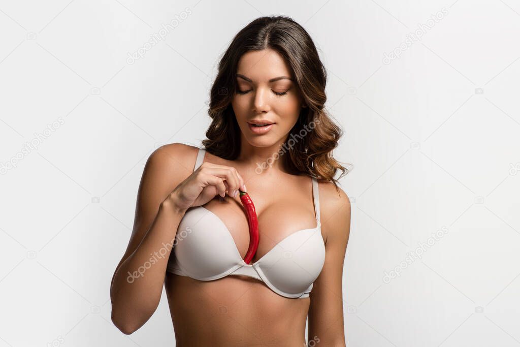 pensive, sexy girl holding red hot chili pepper near big breasts isolated on white