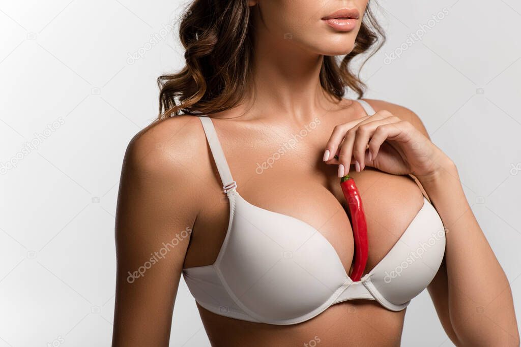 partial view of girl with holding red hot chili pepper between big breasts isolated on white, panoramic shot