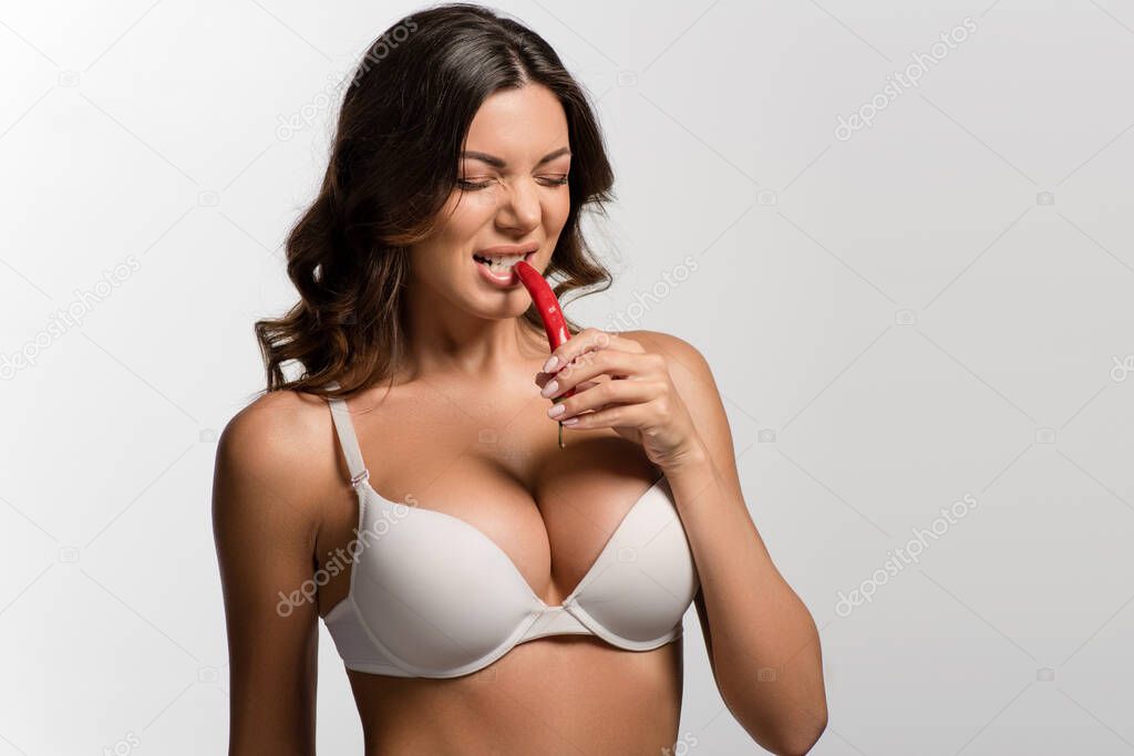 sexy girl with big breasts grimacing while tasting red hot chili pepper isolated on white