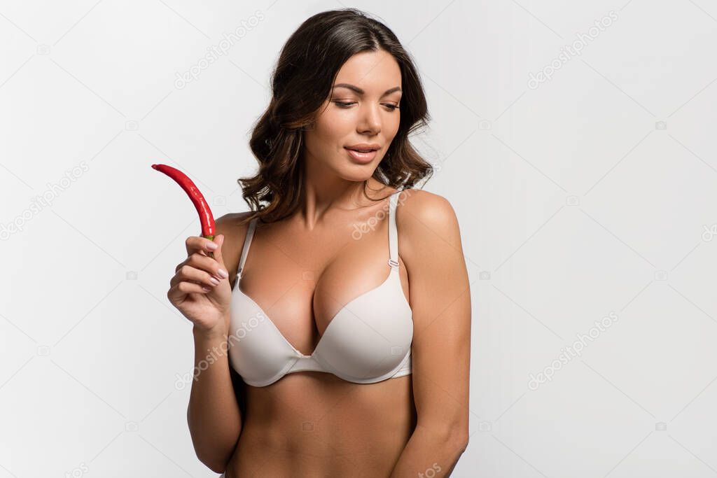 sexy, pensive girl with big breasts holding red hot chili pepper isolated on white