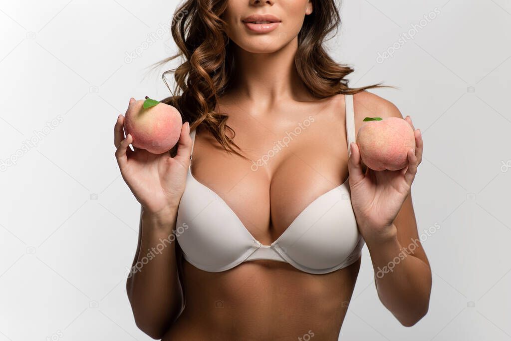 cropped view of sexy girl with big breasts holding ripe peaches isolated on white