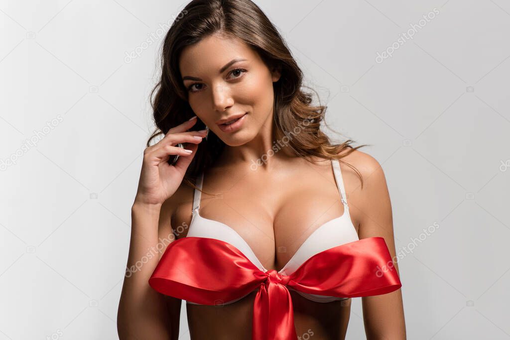 flirty, sexy girl with big breasts and red satin bow on bra looking at camera isolated on white