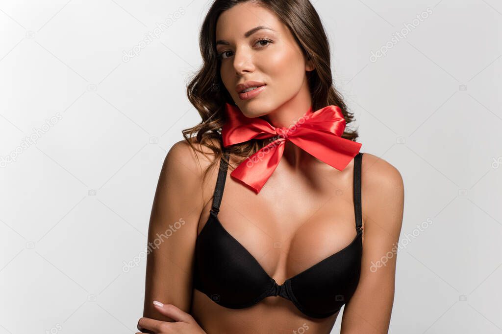 sexy, flirty girl with big breasts and red satin bow on neck looking at camera isolated on white