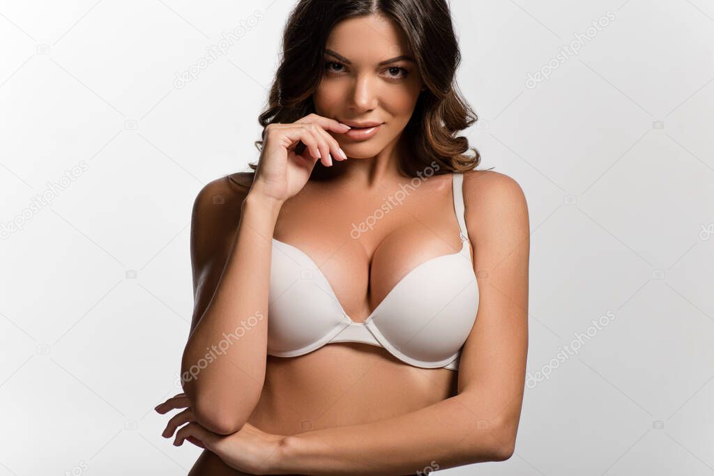 sensual flirty girl with big breasts looking at camera while touching lip isolated on white