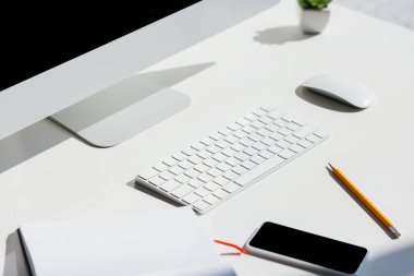 Bilgisayar monitörü, klavyesi ve faresi olan ev ofisi not defteri, kalem ve akıllı telefonlu masada.