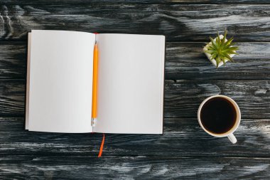 Boş not defteri, kalem, kahve fincanı ve koyu ahşap yüzeyin üst görüntüsü.
