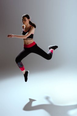 Gri üzerine atlayan spor giyimli çekici kız. 