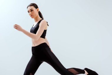 Siyah spor giyim giymiş güzel bir kadın beyazlar üzerinde tek başına egzersiz yapıyor. 