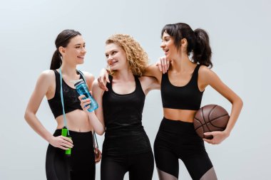 Neşeli ve çok kültürlü kızlar spor malzemeleriyle beyazların üzerinde dikiliyorlar. 