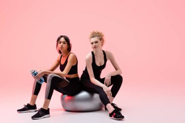 Sportif kız spor salonunda elinde pembe şişeyle Afro-Amerikan bir kadınla oturuyor. 