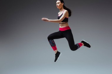 Gri üzerine atlayan spor giyimli genç ve güzel bir kadın.