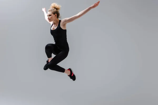 Uzamış Elleri Olan Kıvırcık Sporcu Kadın Gri Renkte Zıplıyor — Stok fotoğraf
