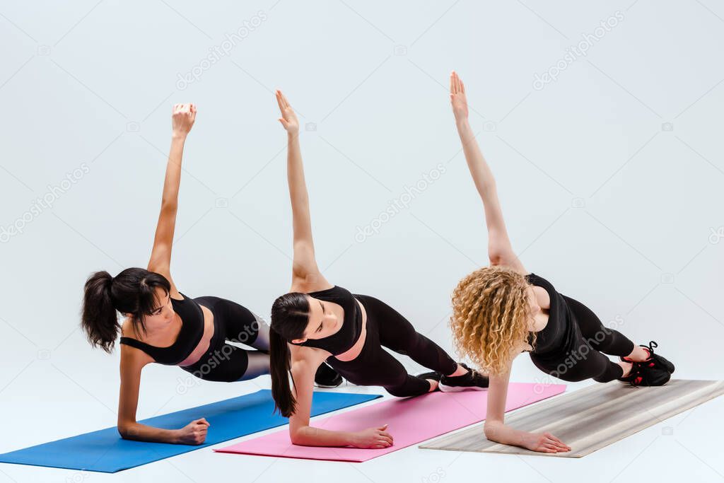 multicultural women with outstretched hands exercising on fitness mats isolated on white 