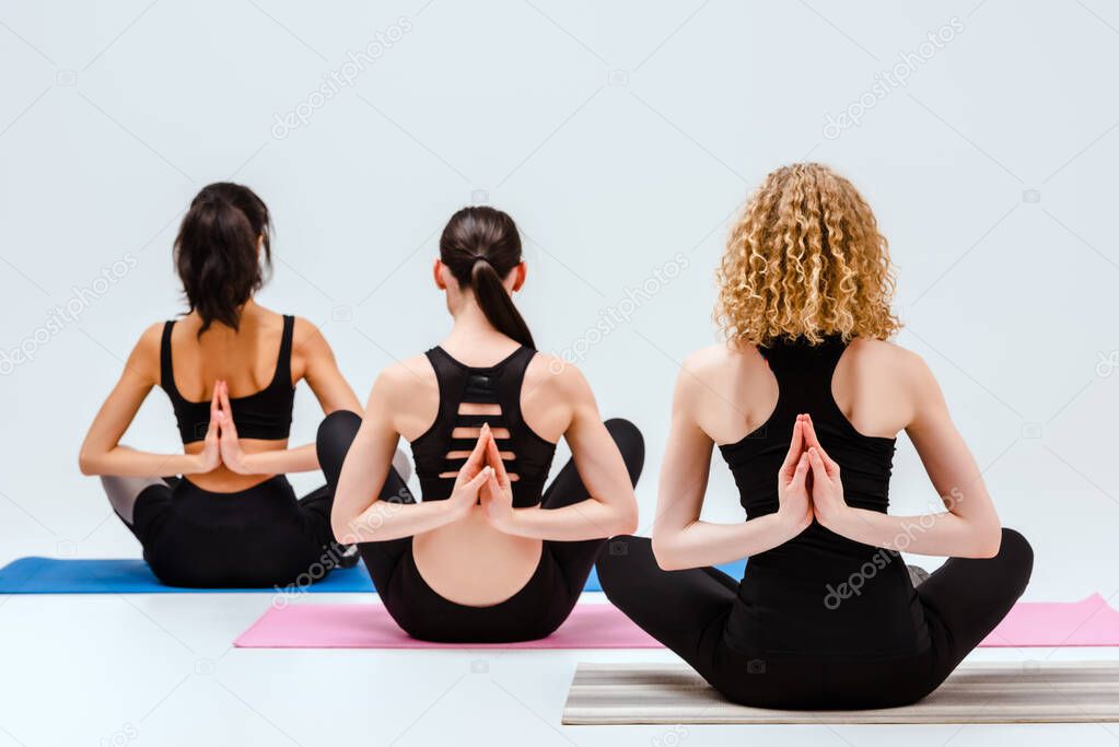 back view of women in reverse prayer pose on yoga mats isolated on white 