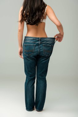 back view of girl touching oversized jeans and standing on grey  clipart