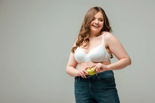 穿着牛仔裤和胸罩的快乐而又大的女孩 手里拿着一个灰色的苹果 — 图库照片