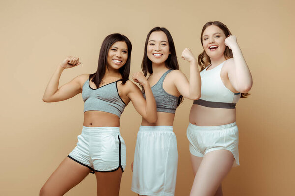 Happy sportswomen smiling and looking at camera on beige