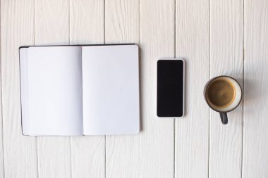 Kahvenin üst görüntüsü, akıllı telefon ve ahşap arka plandaki defter.