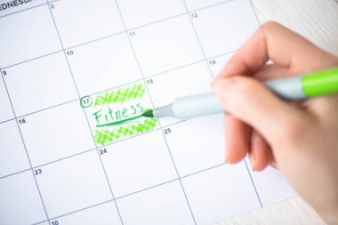 Cropped view of woman pointing with marker pen on fitness lettering in to-do calendar on wooden background clipart