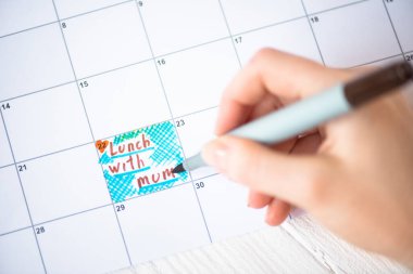 Cropped view of woman pointing with marker pen on lunch with mum lettering in to-do calendar on wooden background clipart