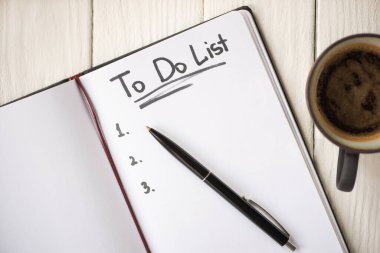 Not defterinin en üst görünümü. Liste harfleri ve tahta arka planda kahve fincanının yanındaki kalem.