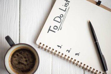 Top view of notebook with do list lettering and pen with cup of coffee on wooden background clipart