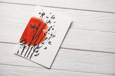 Japon resimli kağıdın üst görüntüsü kırmızı güneş ve ahşap arka planda dallar.