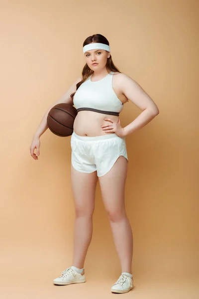 Deportista Talla Grande Con Mano Cadera Pelota Mirando Cámara Beige — Foto de Stock