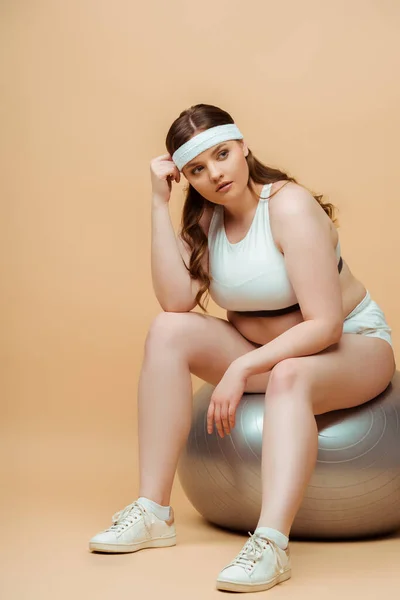 Size Sportswoman Olhando Para Longe Sentado Bola Fitness Fundo Bege — Fotografia de Stock