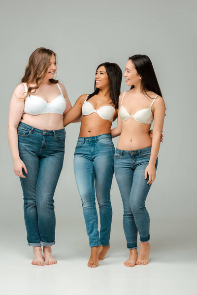 Мультикультурные женщины обнимаются, улыбаются и смотрят друг на друга на сером фоне
