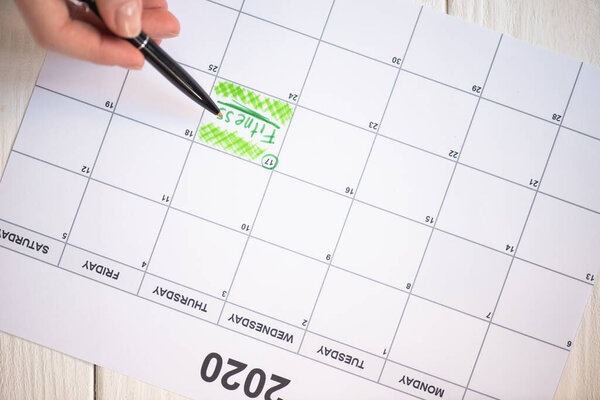 Cropped view of woman pointing with pen on fitness lettering in to-do calendar with 2020 inscription on wooden background