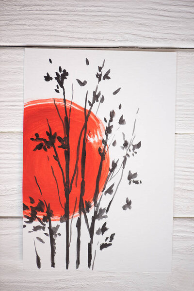 Top view of paper with Japanese painting with red sun and branches on wooden background