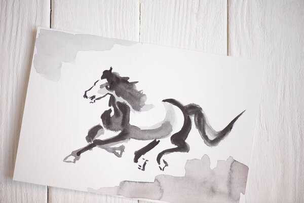 Top view of paper with Japanese painting with horse on wooden background