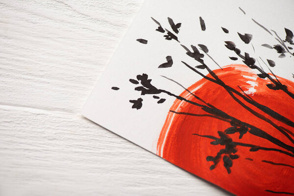 Top view of paper with Japanese painting with red sun and branches on wooden background