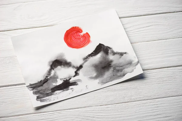 Top view of paper with Japanese painting with hills and red sun on wooden background