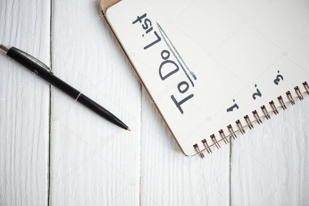 Top view of notebook with do list lettering with pen on wooden background