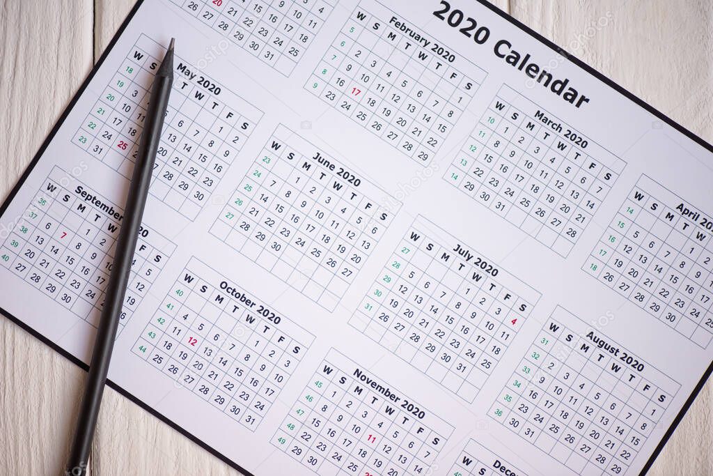 Top view of 2020 calendar and pencil on wooden background