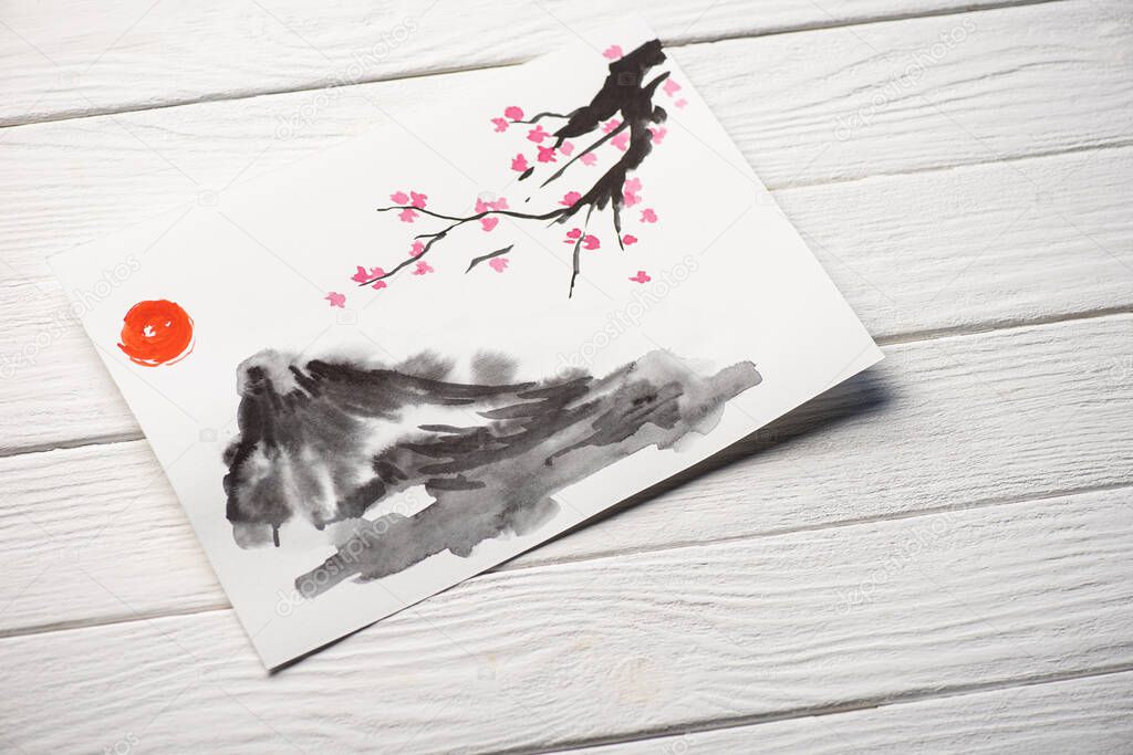 High angle view of paper with japanese painting with sun, Sakura branches and grey hill on wooden background
