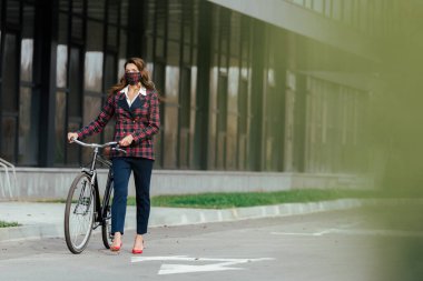 Ekose maskeli iş kadınının seçici odağı bisikletle yürüyor 