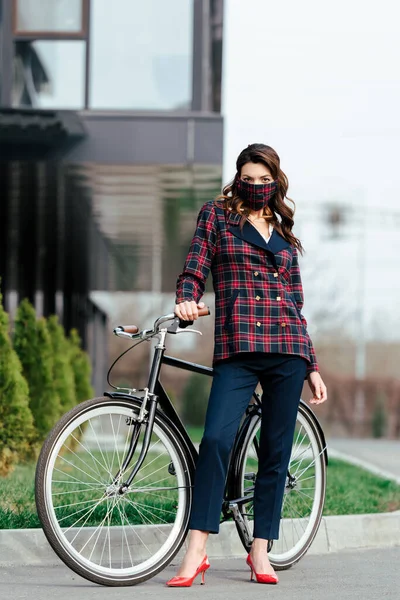 businesswoman in plaid mask standing near bicycle