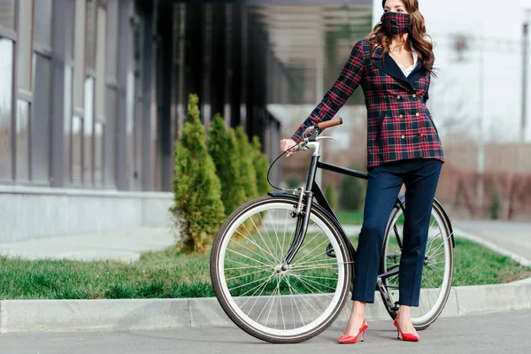 戴着格子呢面具的女商人站在自行车旁边 望着别处 — 图库照片