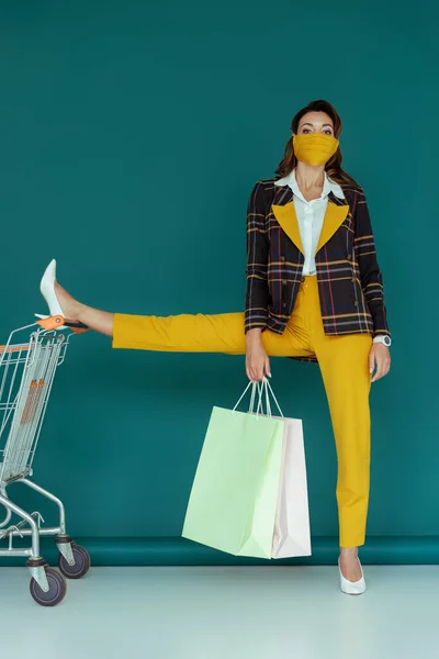Stylish Woman Yellow Mask Putting Leg Shopping Cart While Holding — Stock Photo, Image